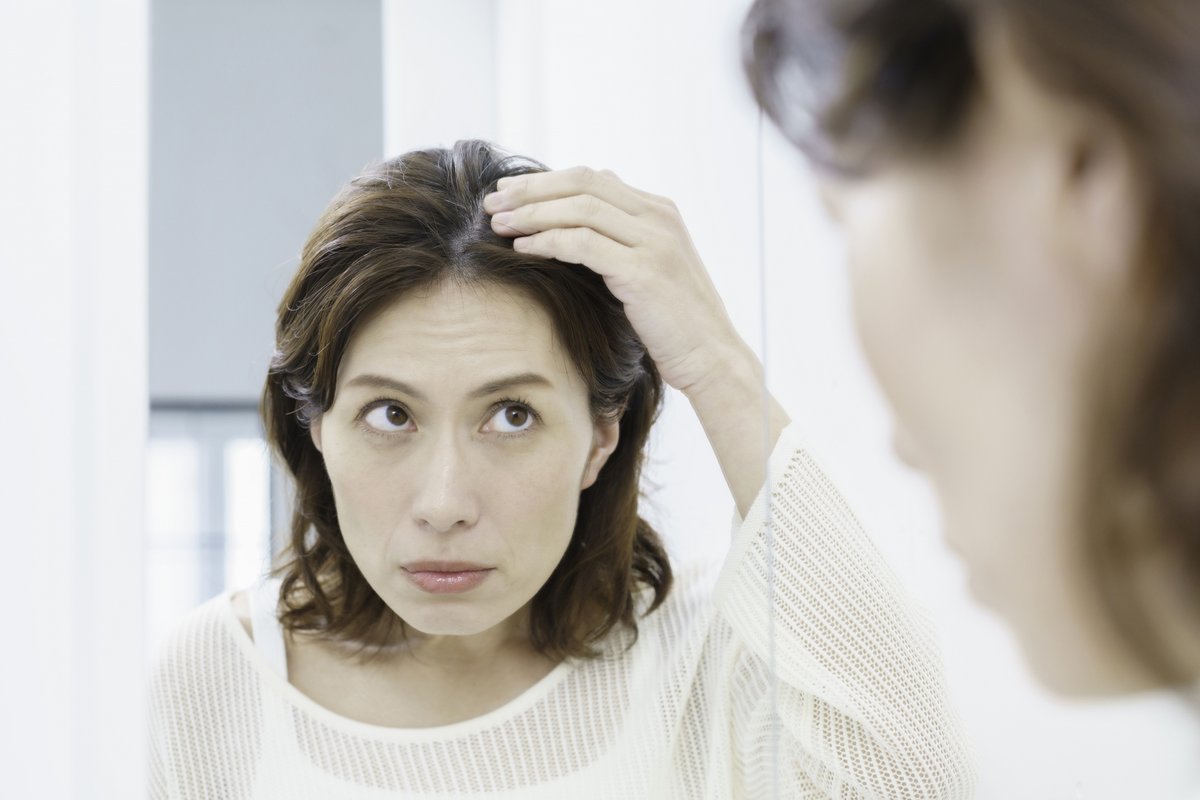 鏡を見て分け目を気にする女性